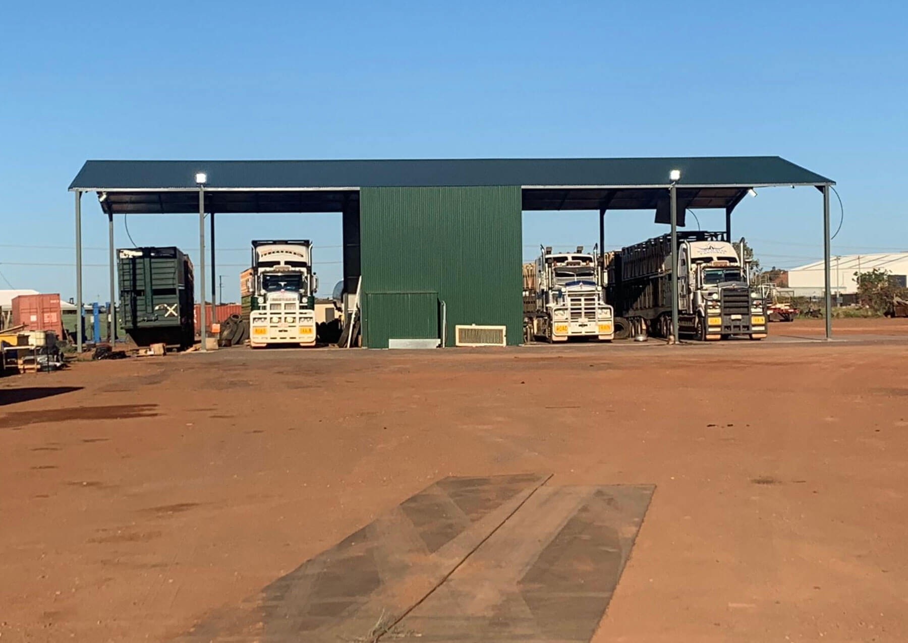 Open-bay steel shed sheltering road train trucks